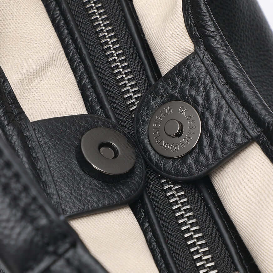 Close-up of a black leather bag with zipper and button details.