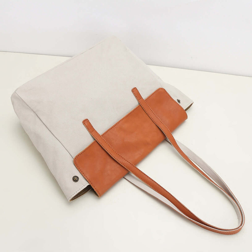 Canvas tote bag flat lay with tan leather flap detail.