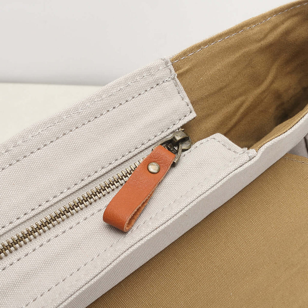 Close-up of a white canvas bag with a zipper and brown leather pull tab.