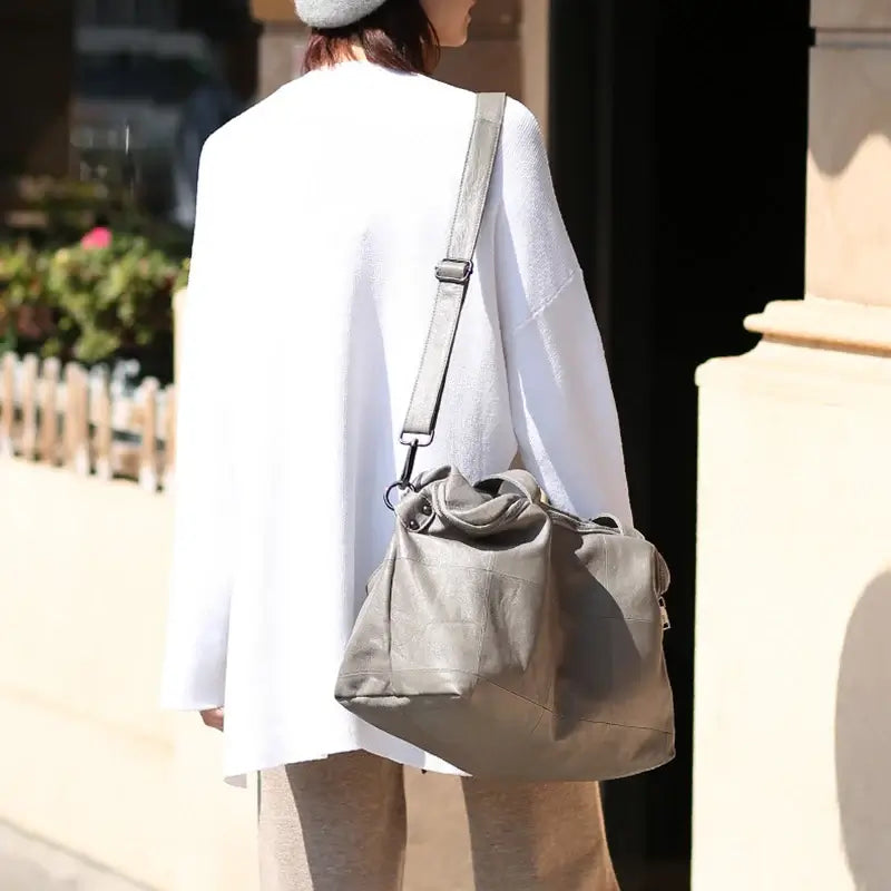 Person wearing a white coat and beige pants with a gray shoulder bag on a city street.