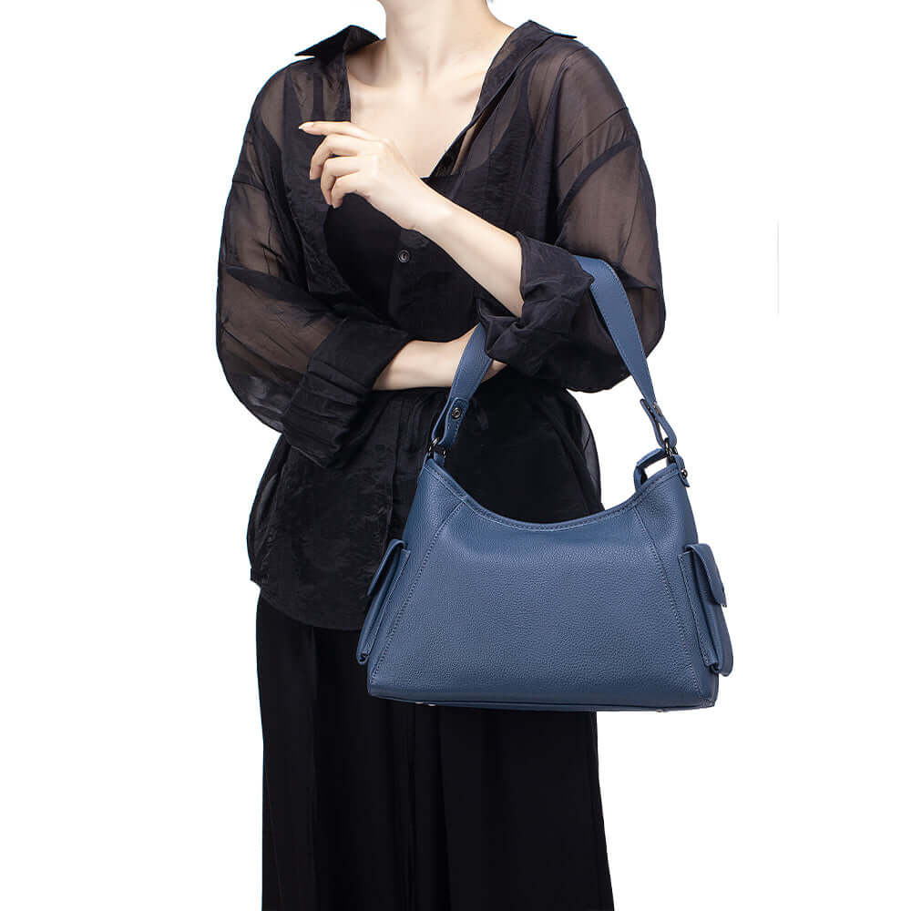 Model holding blue leather shoulder bag in casual outfit.