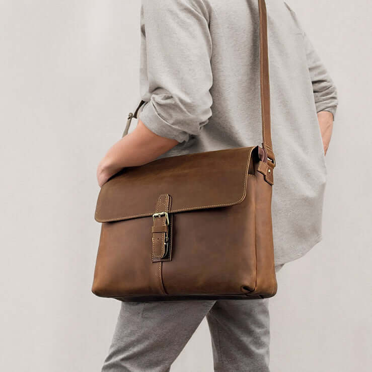 Man carrying brown leather messenger bag in crossbody style.