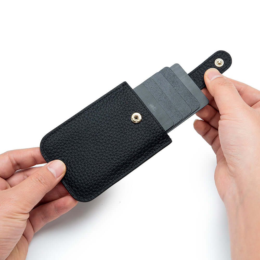 Slim black leather card holder held in hand showing compact size.