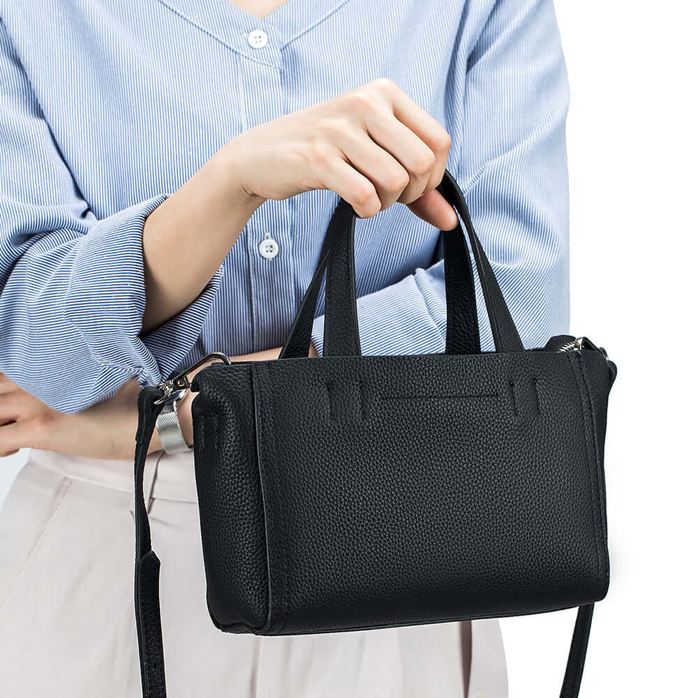 Model holding black mini leather handbag by handle – perfect for daily or office use.