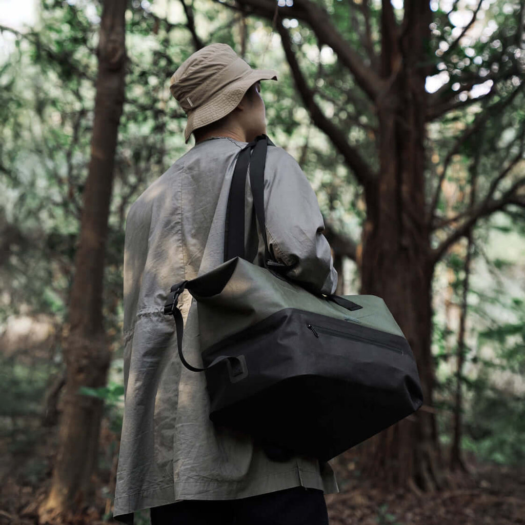 Waterproof duffle bag carried by a man hiking through a forest.