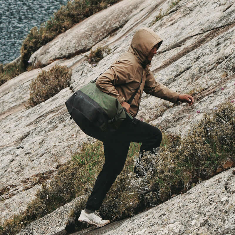 Waterproof duffle bag carried by a hiker on a mountain trail.