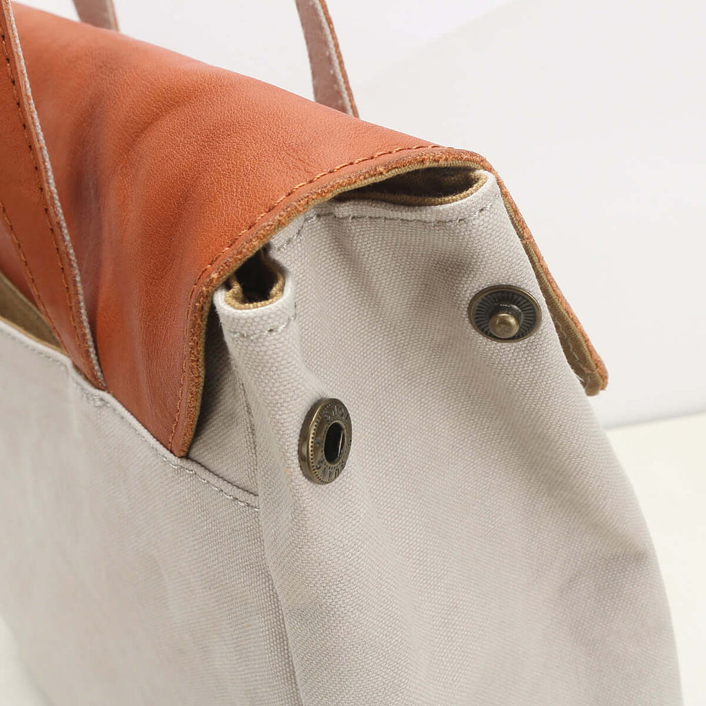 Close-up of a white tote bag with brown leather accents.