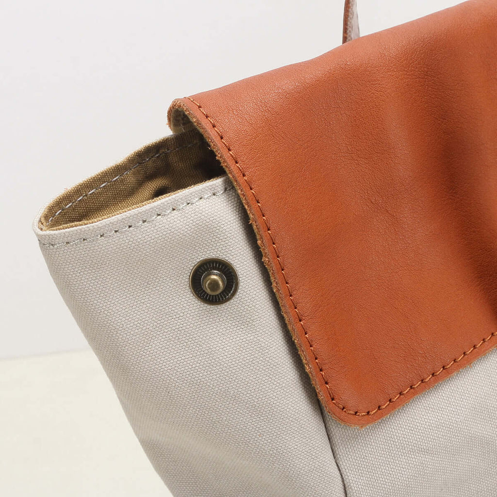 Close-up of a white and brown leather bag with a metal button.